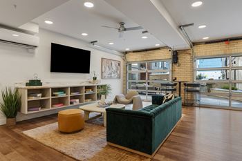 A living room with a green couch, a yellow ottoman, and a flat screen tv mounted on the wall.